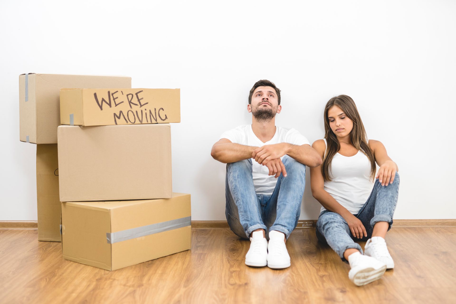 A man and a woman are sitting on the floor next to moving boxes.