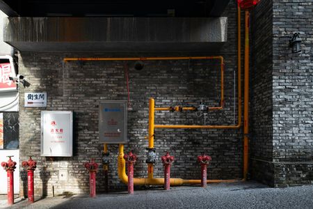 A brick wall with yellow pipes and red fire hydrants.