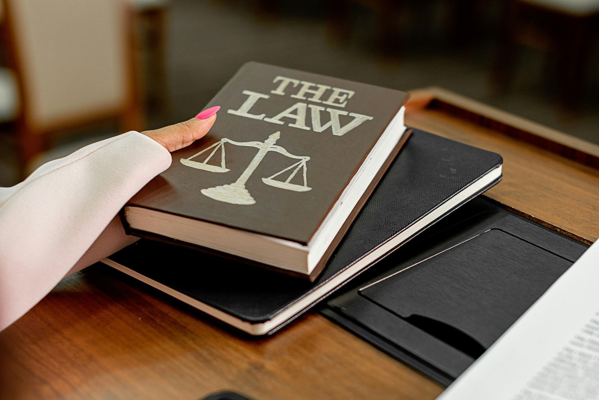 A person holds a brown book titled THE LAW featuring a scale of justice emblem above two stacked black notebooks.