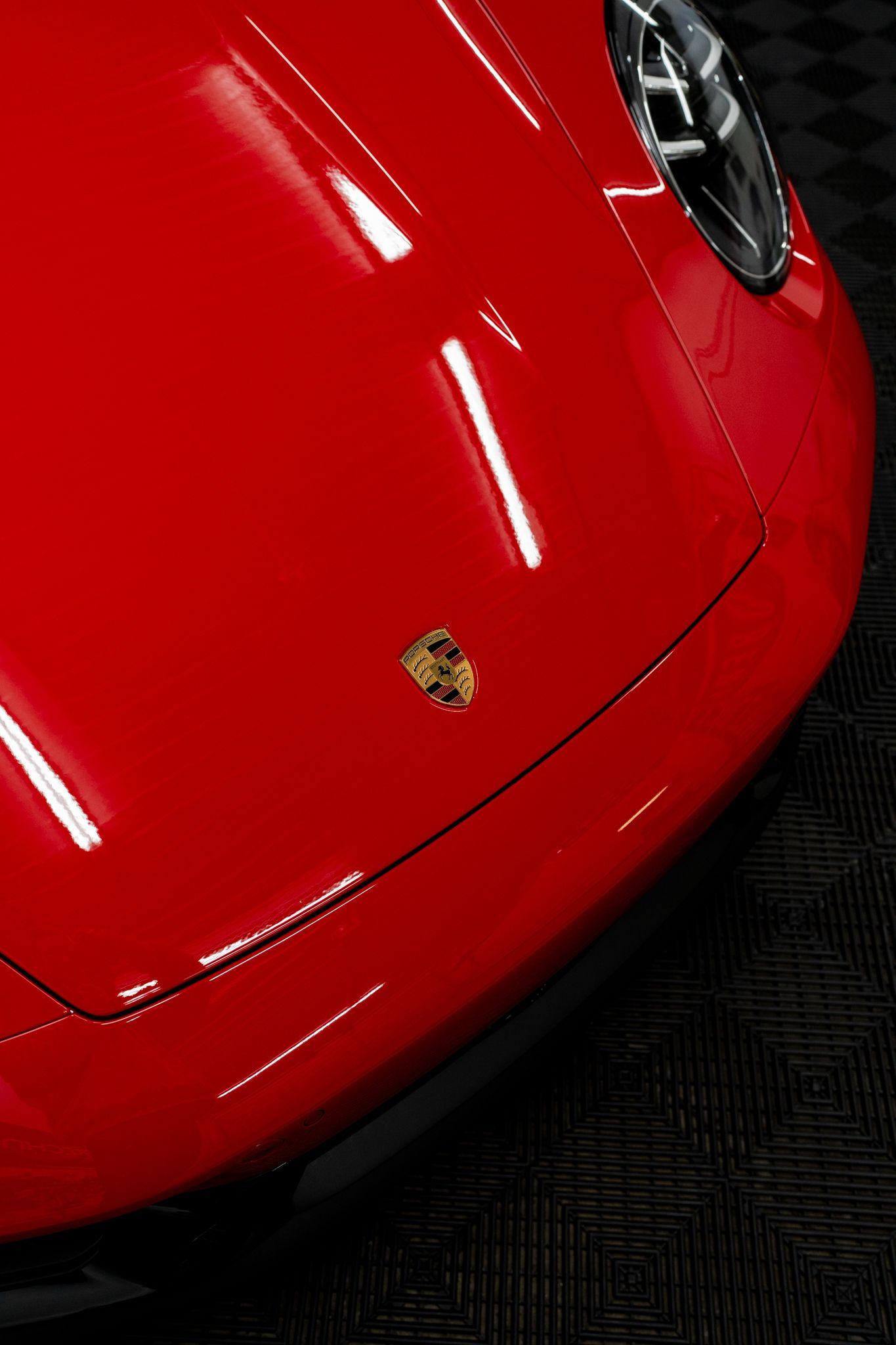 Red Porsche front hood with emblem, reflecting overhead lights.