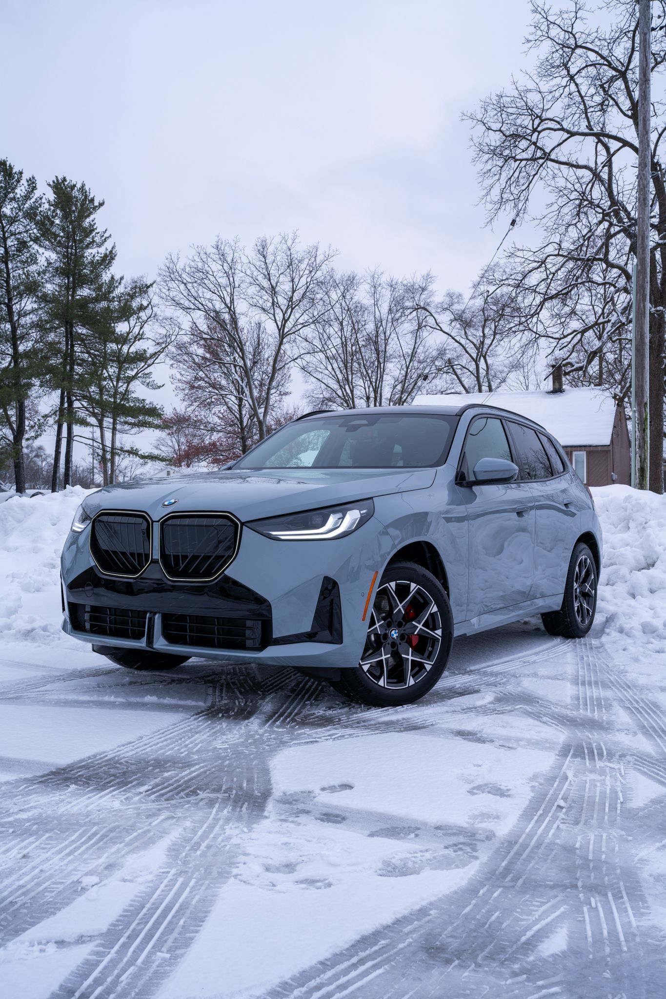 Gray BMW SUV parked in snow-covered area with tire tracks.