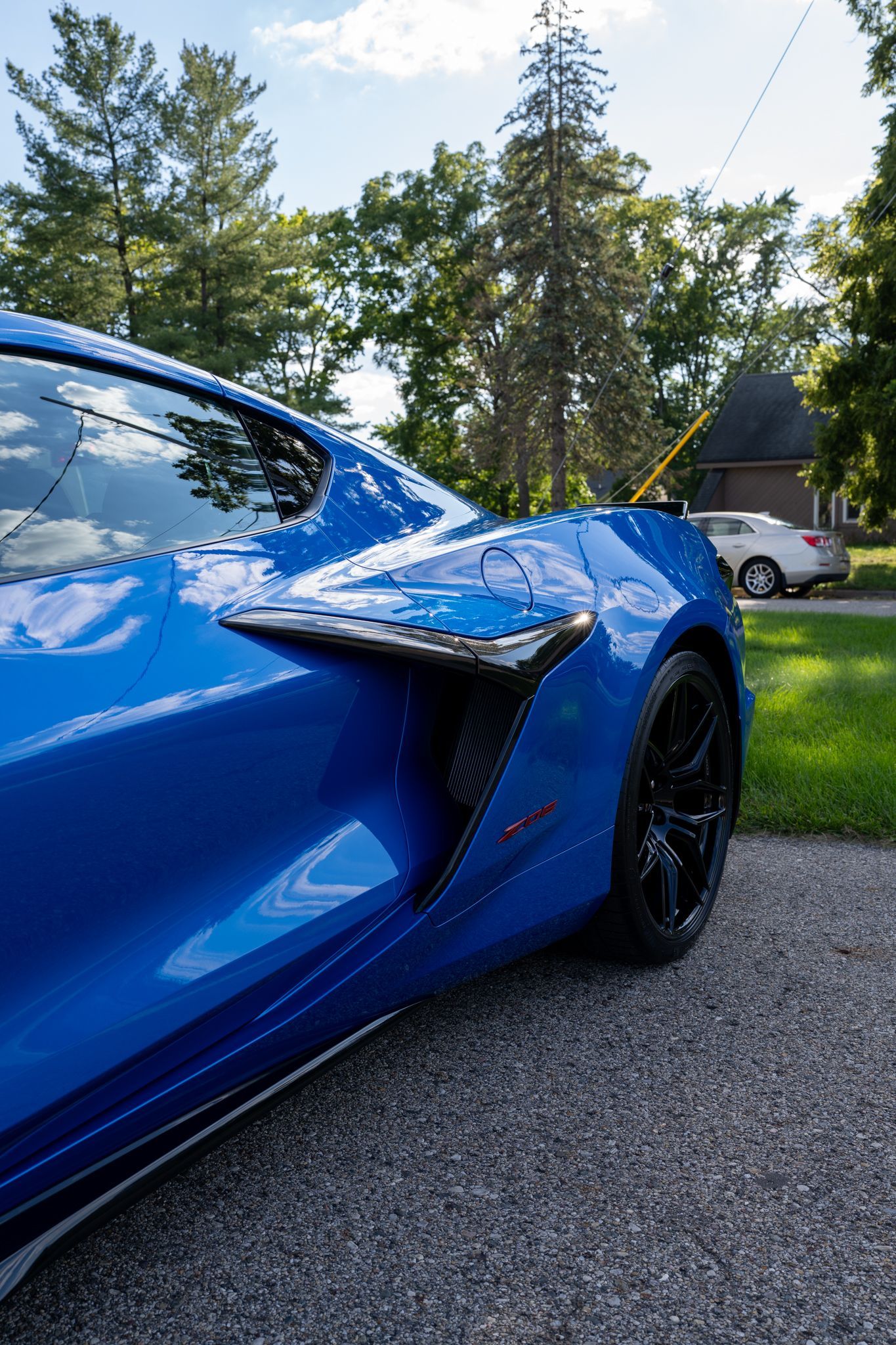 Blue sports car parked on a driveway with a dark wheel. Trees in background.