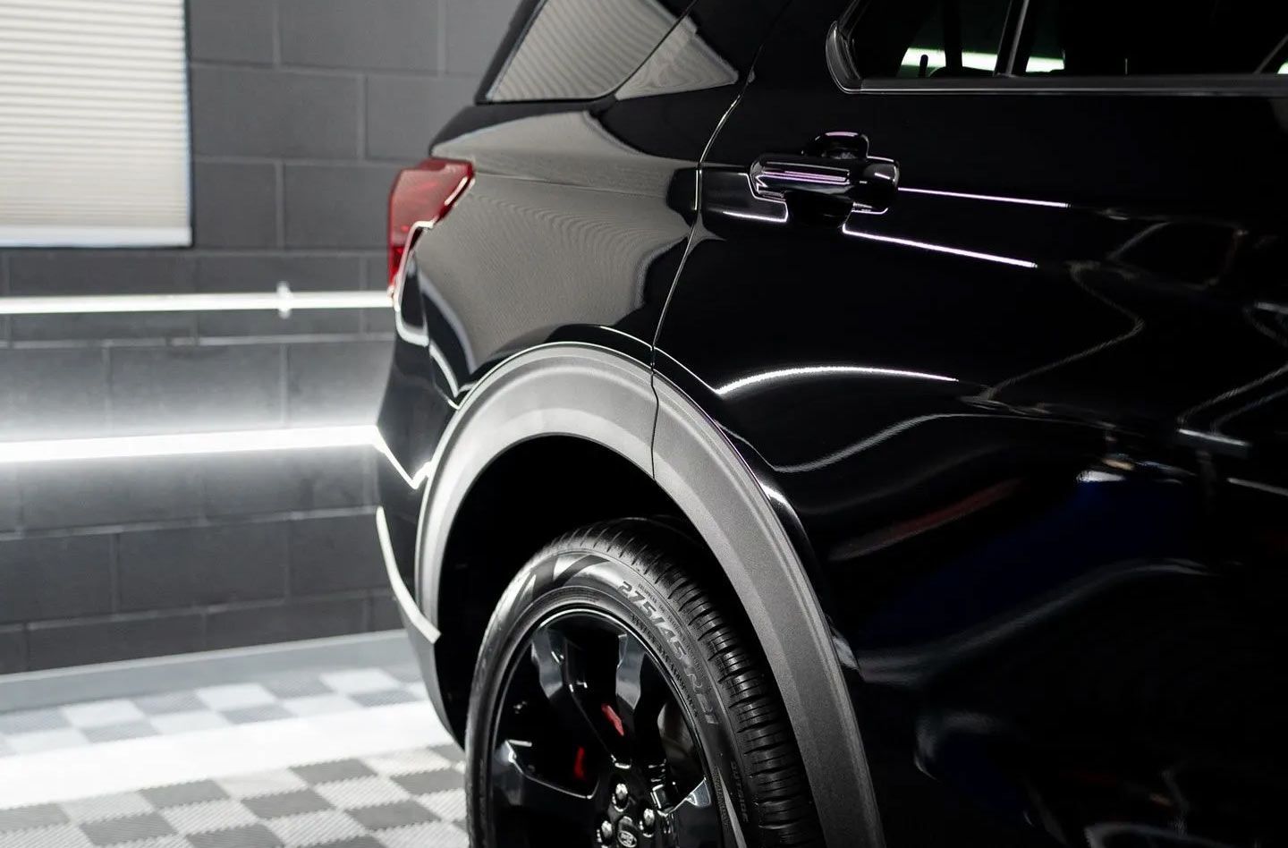 A black car is parked in a garage with a checkered floor.