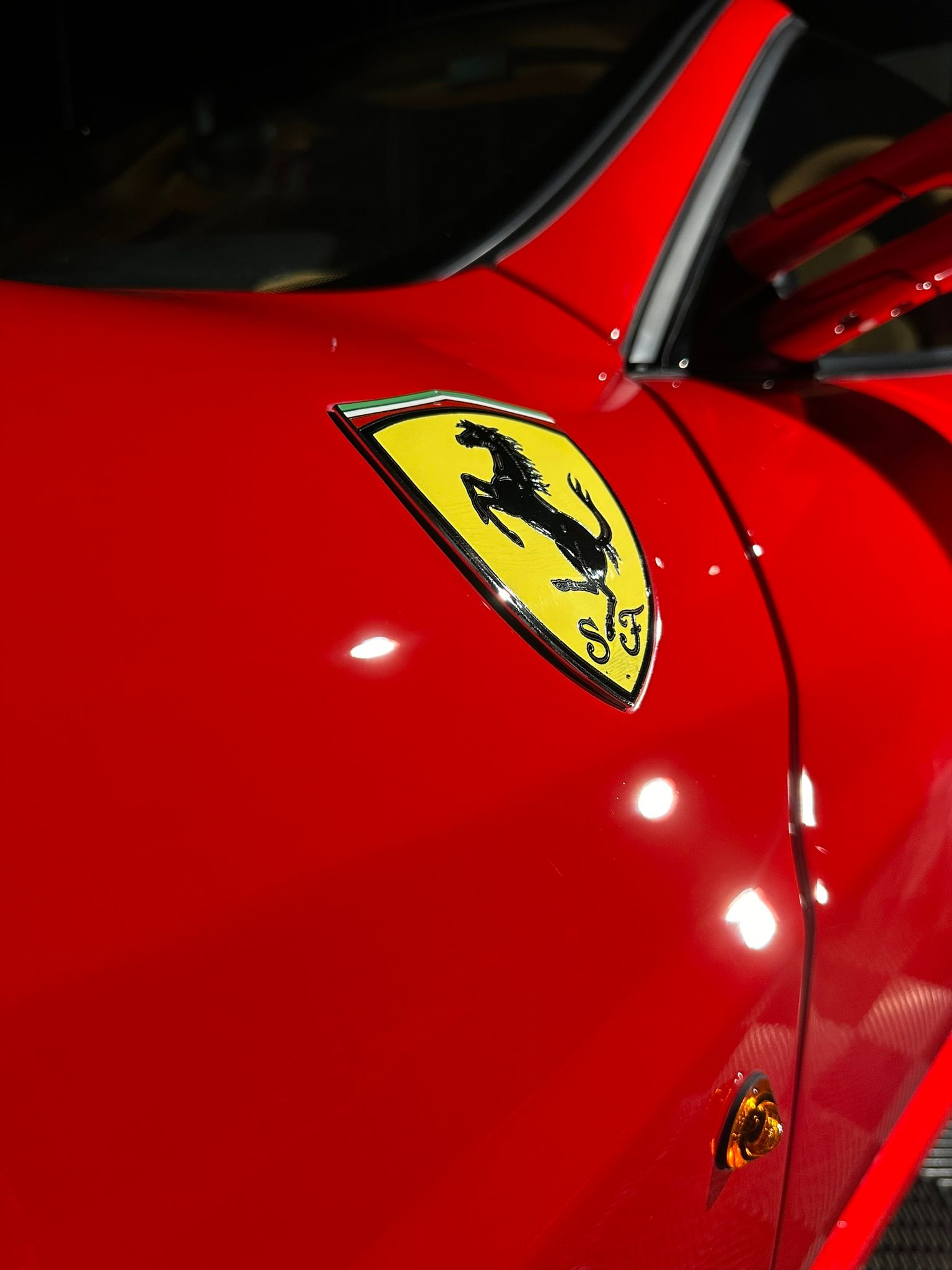 Close-up of a red Ferrari car body with the yellow prancing horse logo.