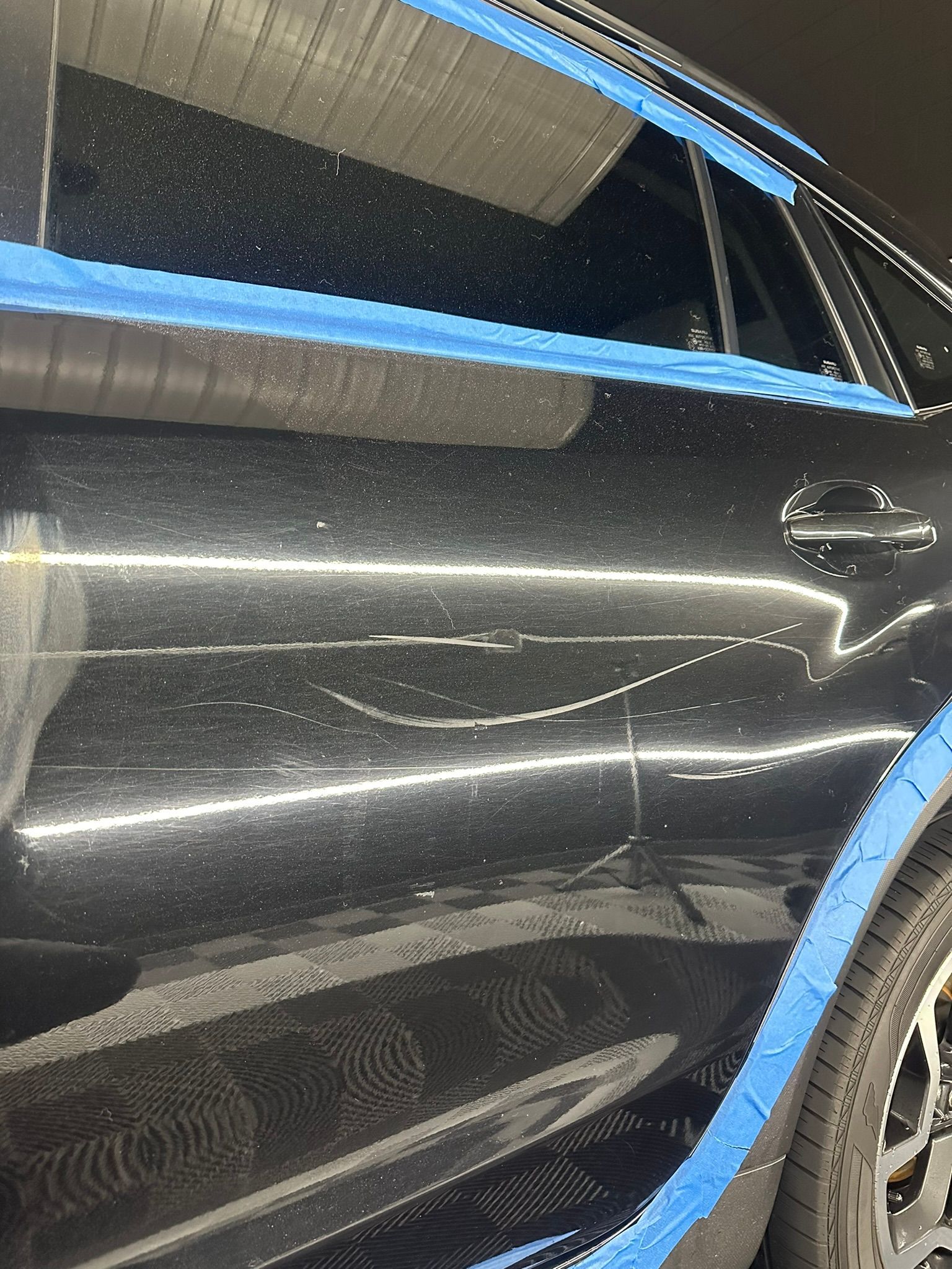 A black car with blue tape on it is sitting in a garage.