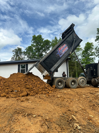 A dump truck is dumping dirt into a pile in front of a house.