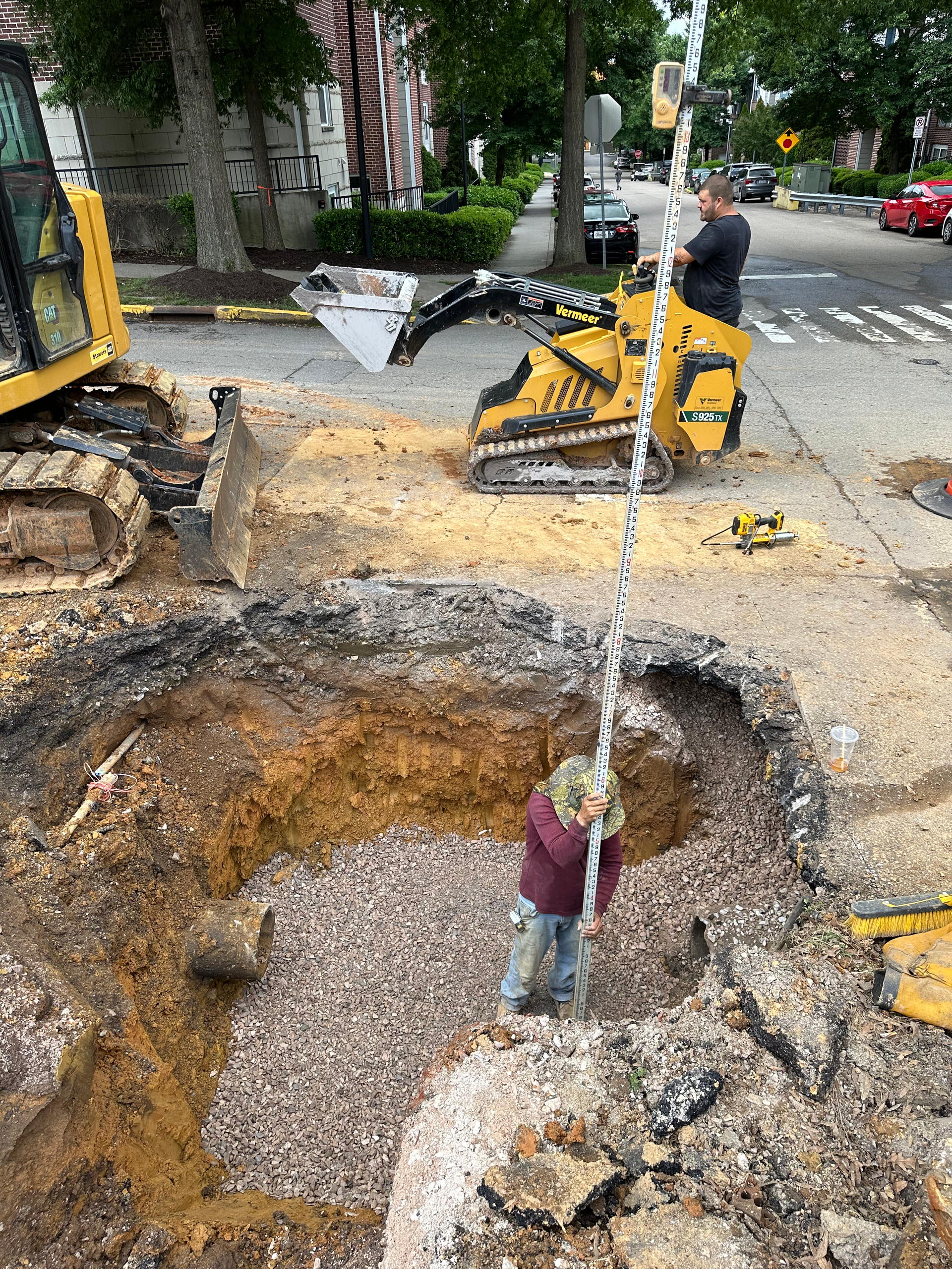 A little girl is standing in a hole in the ground next to a bulldozer.