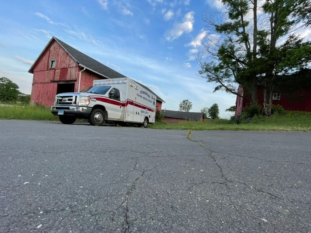 A Simsbury ambulance is parked on the side of the road in front of a barn.