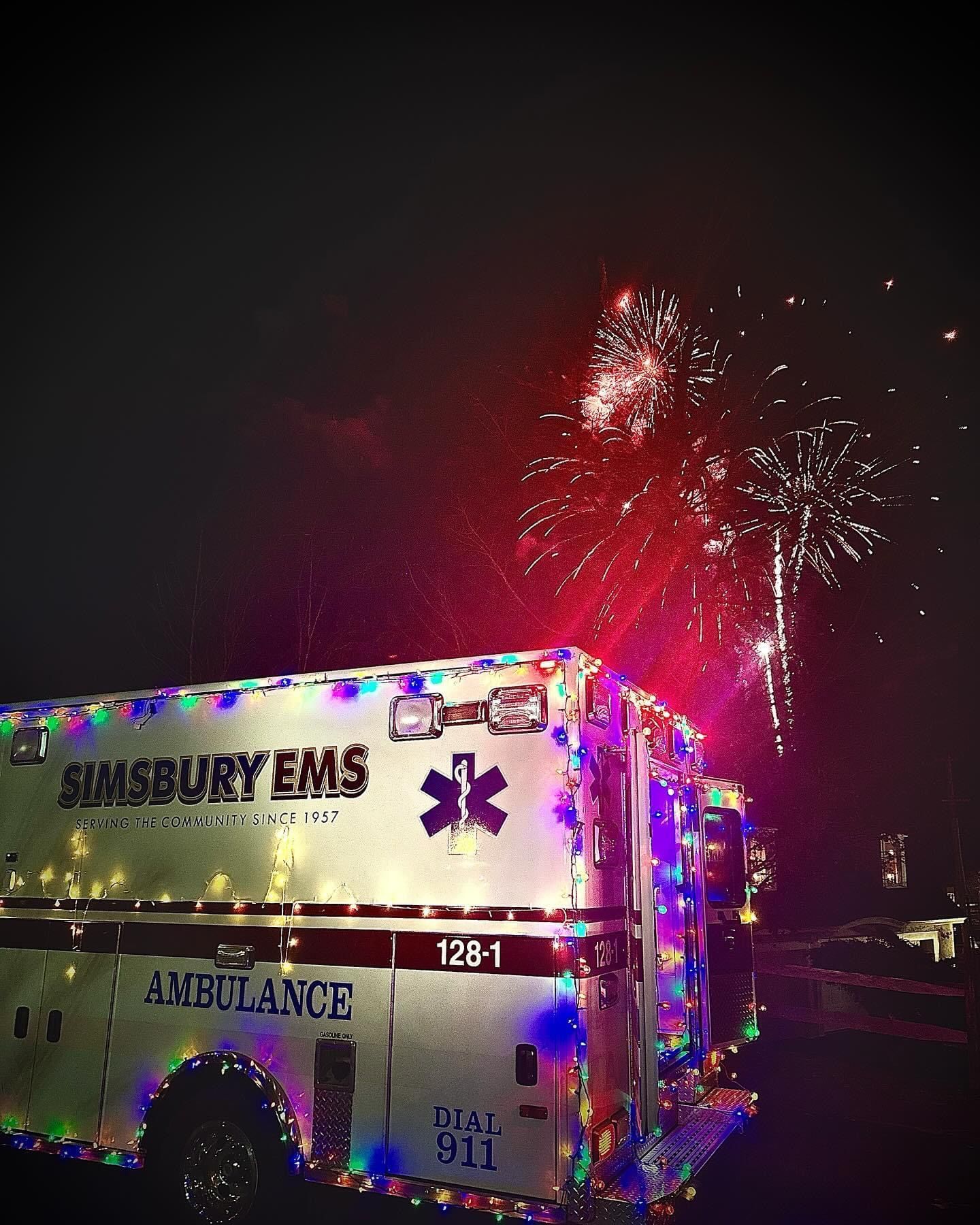 A Simsbury ambulance is decorated with lights and fireworks in the background at Simsbury Celebrates