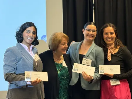 Four people smiling and holding certificates at a formal indoor event