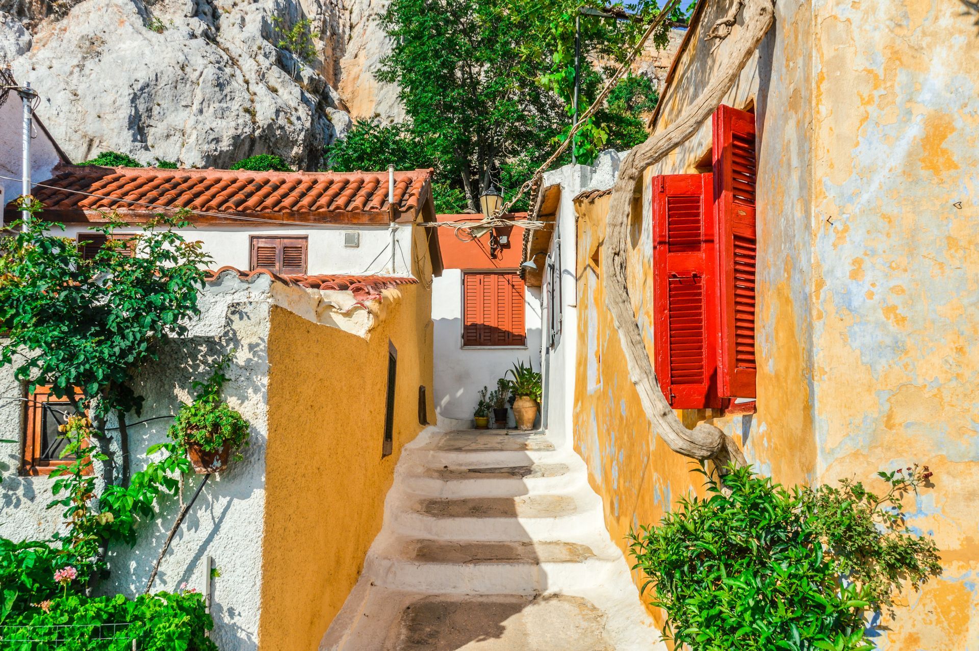 A narrow alleyway between two buildings with red shutters on the windows.