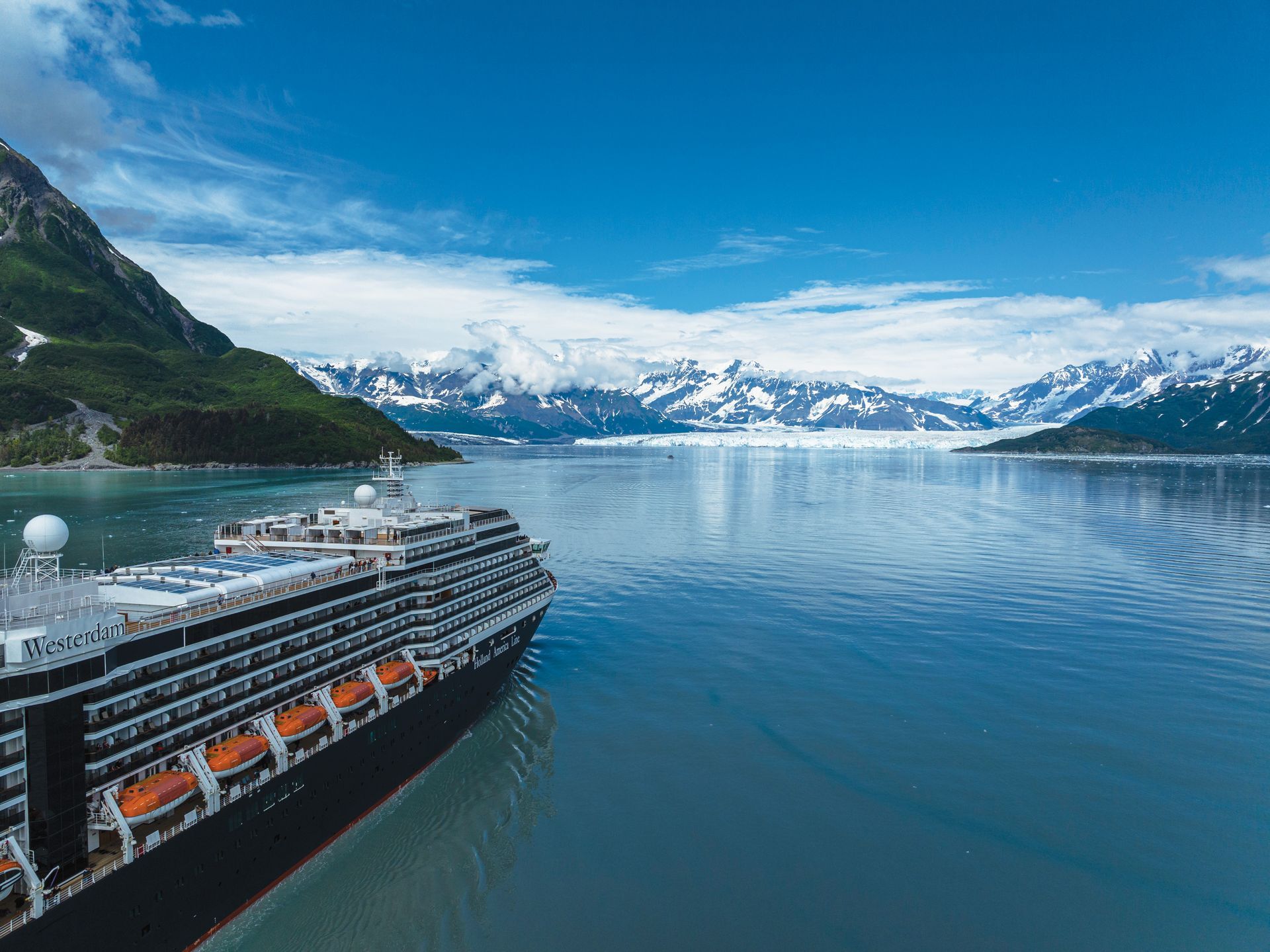 Holland America Line cruise ship is sailing in Alaska with mountains in the background.