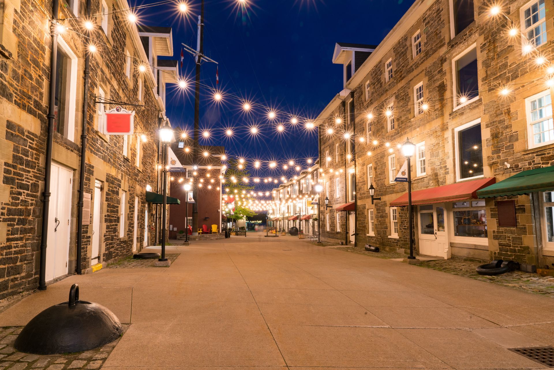 An empty street in Halifax with a string of lights hanging from the buildings at night.