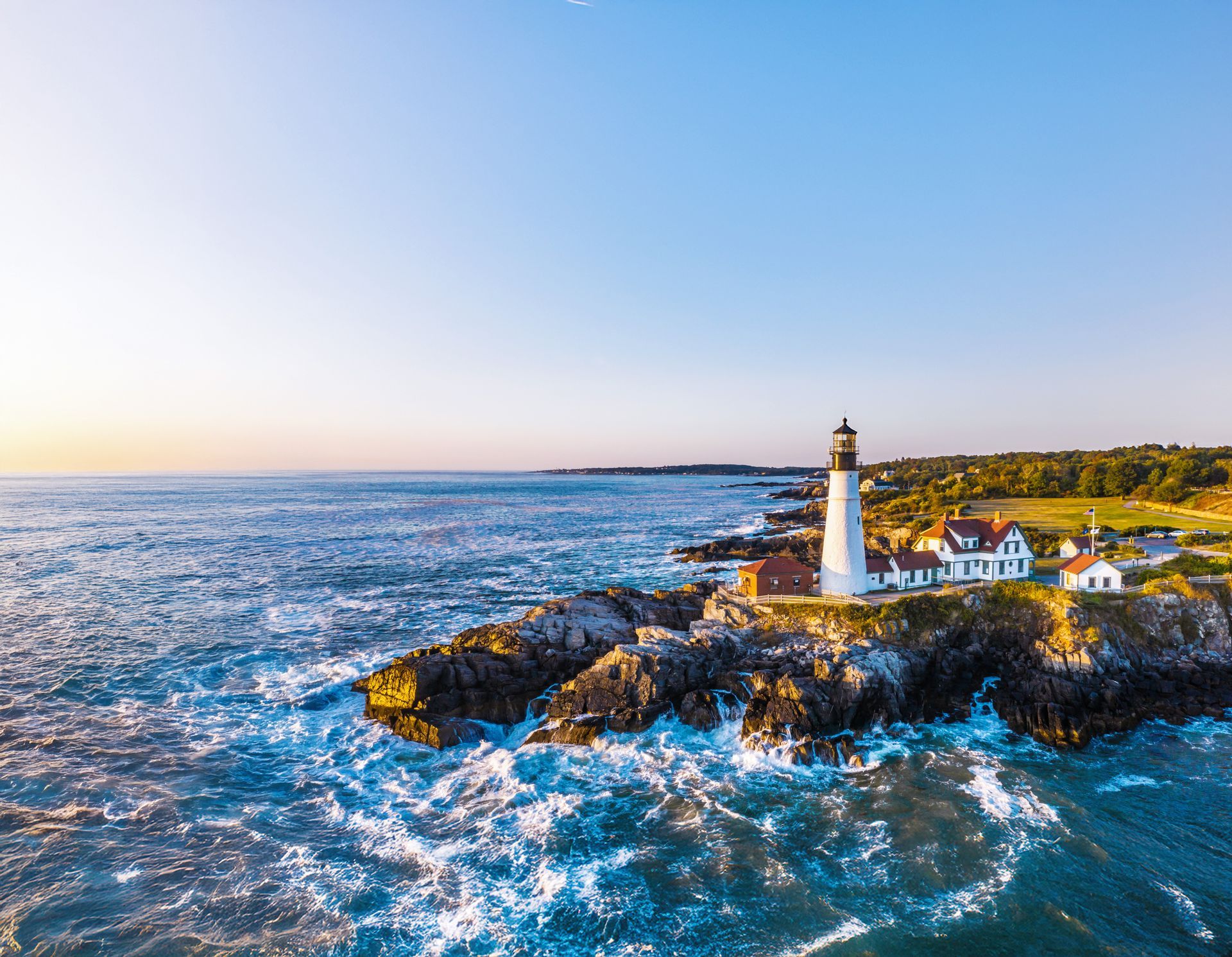 An aerial view of a lighthouse on a rocky cliff overlooking the ocean.