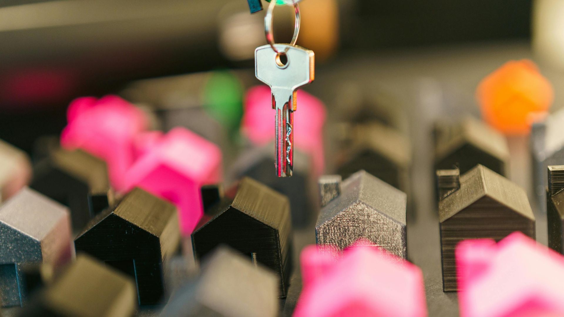 Key hanging above miniature houses, some pink, some gray.