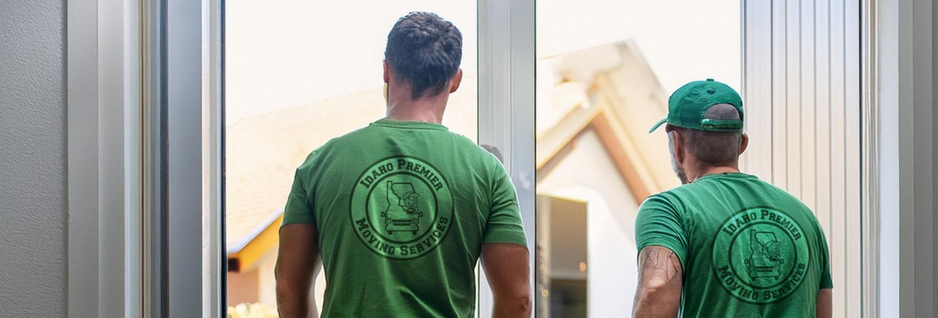 Two people in green shirts stand by an open door looking out at a building.