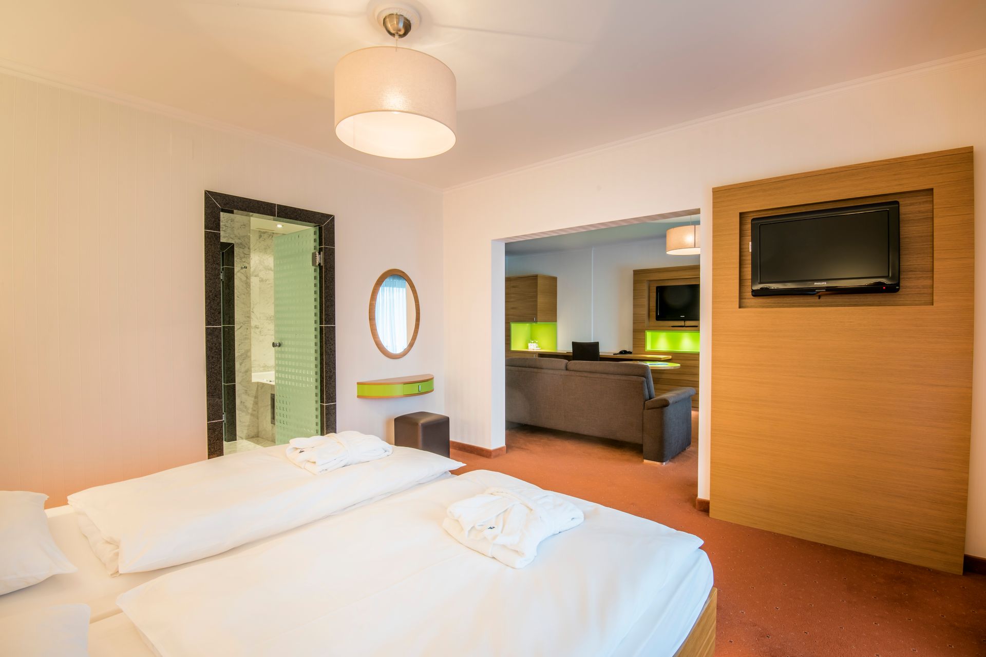 Chambre d'hôtel avec deux lits jumeaux, une télévision et une porte ouverte sur un salon.