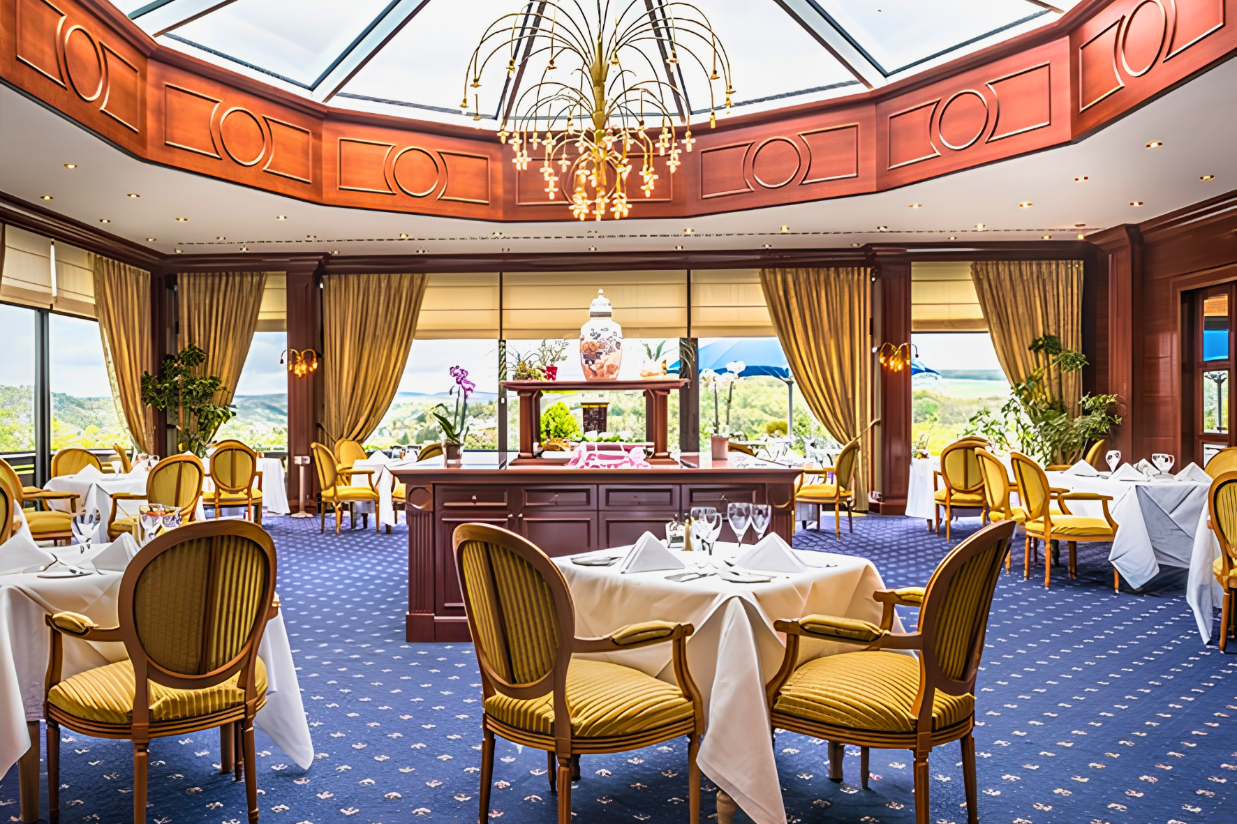 Salle à manger haut de gamme avec chaises jaunes rembourrées, nappes blanches et lustre sous verrière.