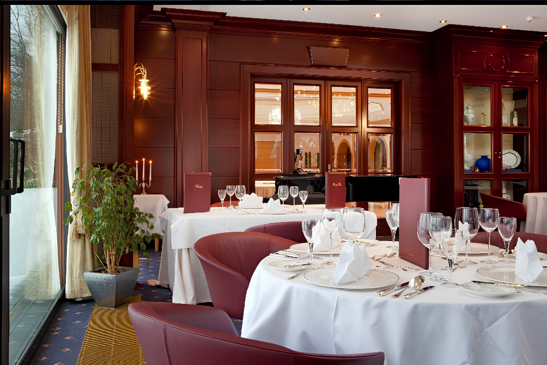 Salle à manger haut de gamme avec boiseries sombres, tables rondes nappées de blanc et fauteuils en cuir bordeaux.