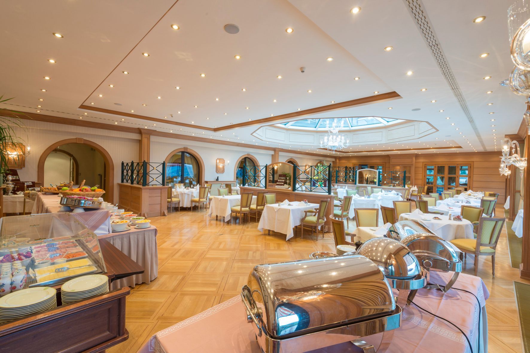 Vue en plongée d’une salle à manger avec réchauds de buffet au premier plan et tables nappées de blanc à l’arrière-plan.