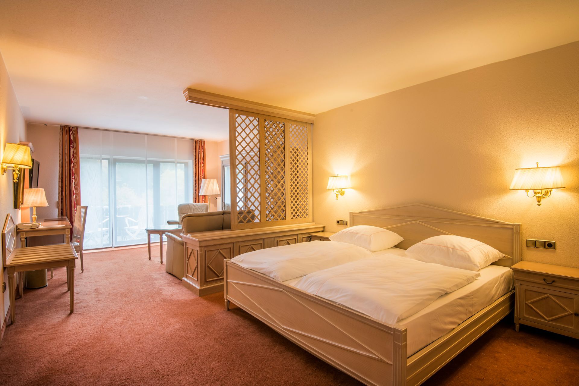 Chambre d'hôtel avec un lit double, un bureau et un coin salon séparés par un paravent décoratif.