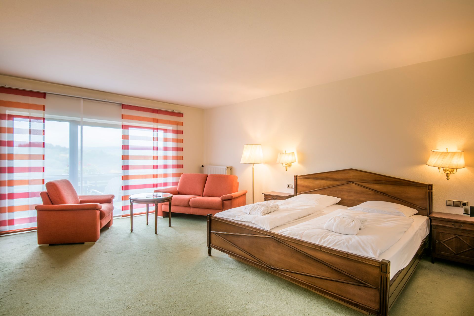 Une chambre d'hôtel avec un lit double, un coin salon et une grande fenêtre avec des rideaux orange.