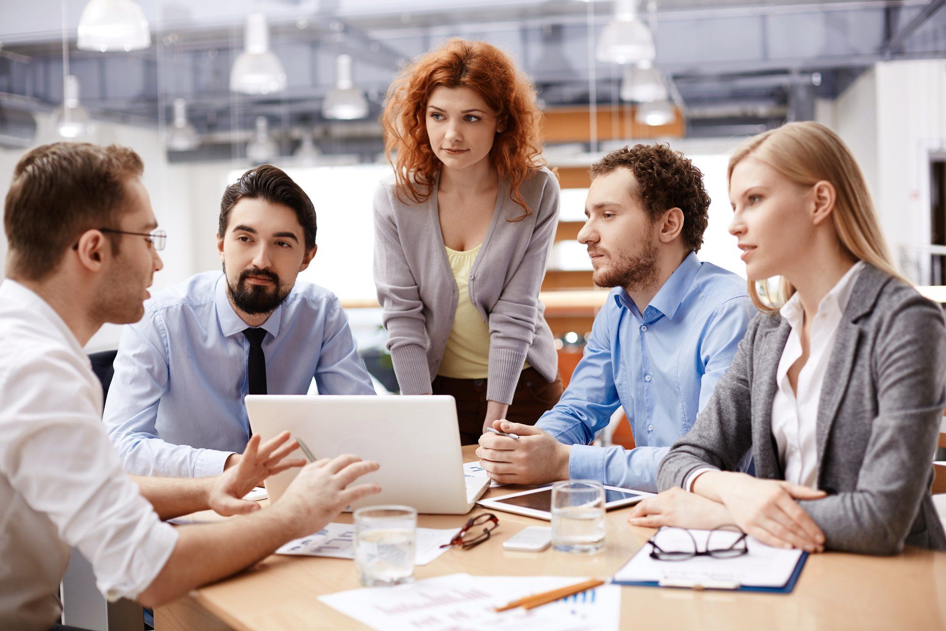 People at a table looking at a laptop, discussing. An office setting with bright lights.