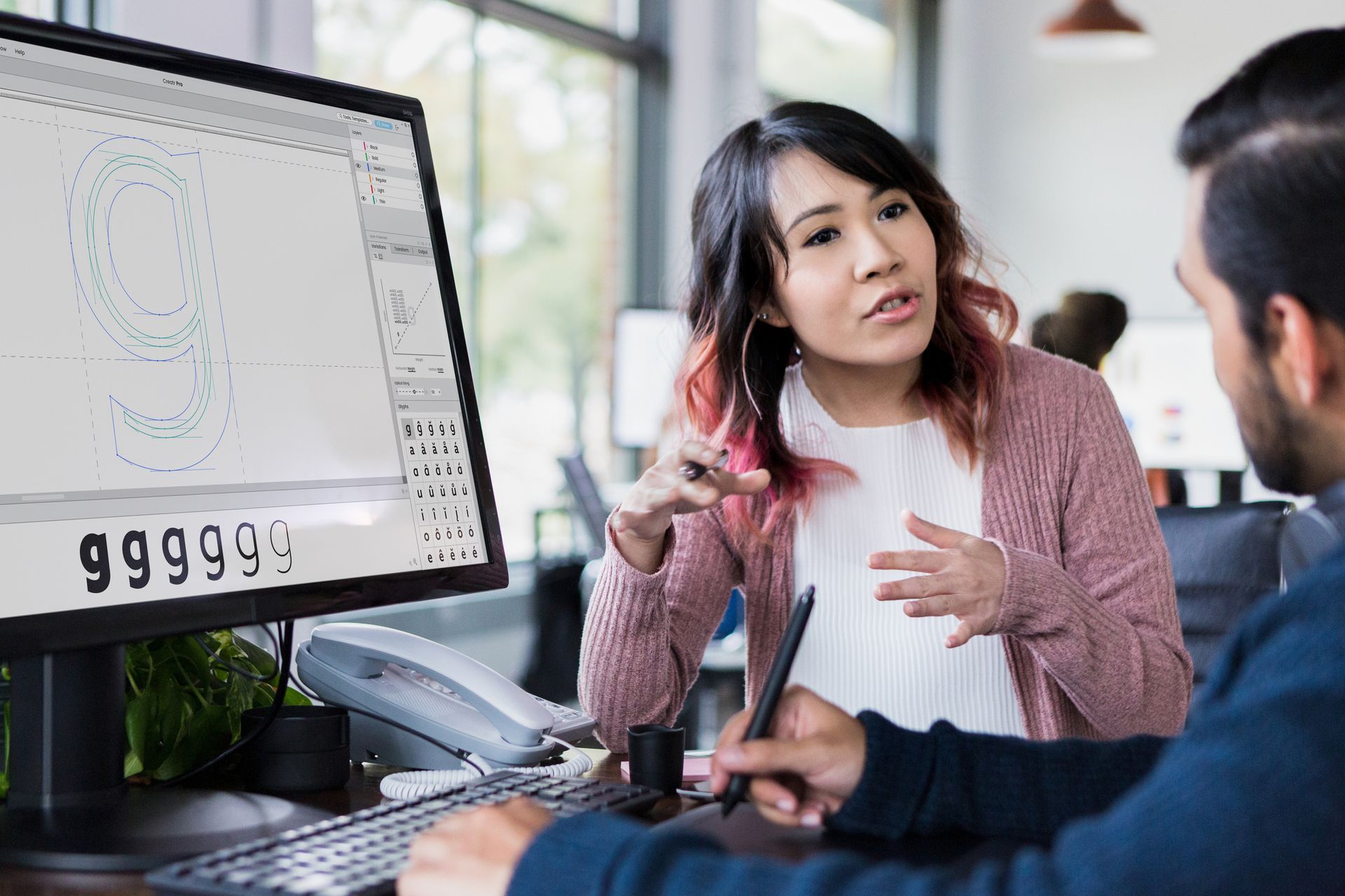 A man and a woman are sitting at a desk in front of a computer.