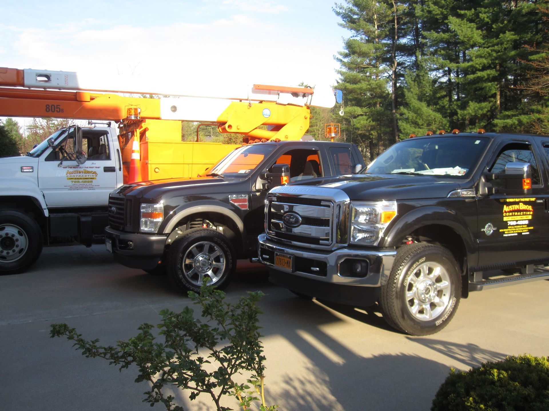 Three work trucks parked outside. One white, two black. Orange lift arm visible in background.