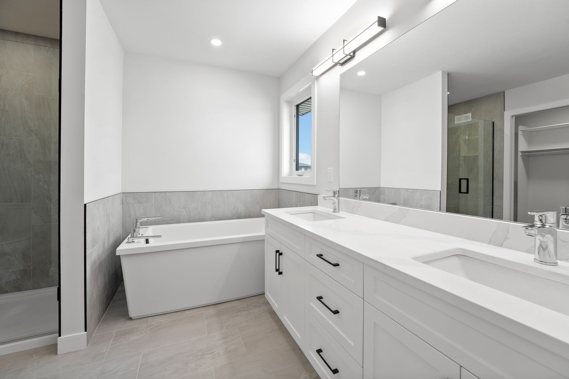 Modern white bathroom with a tub, double vanity, shower, and a window.