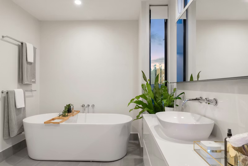 Modern white bathroom with a soaking tub, sink, and leafy plant.