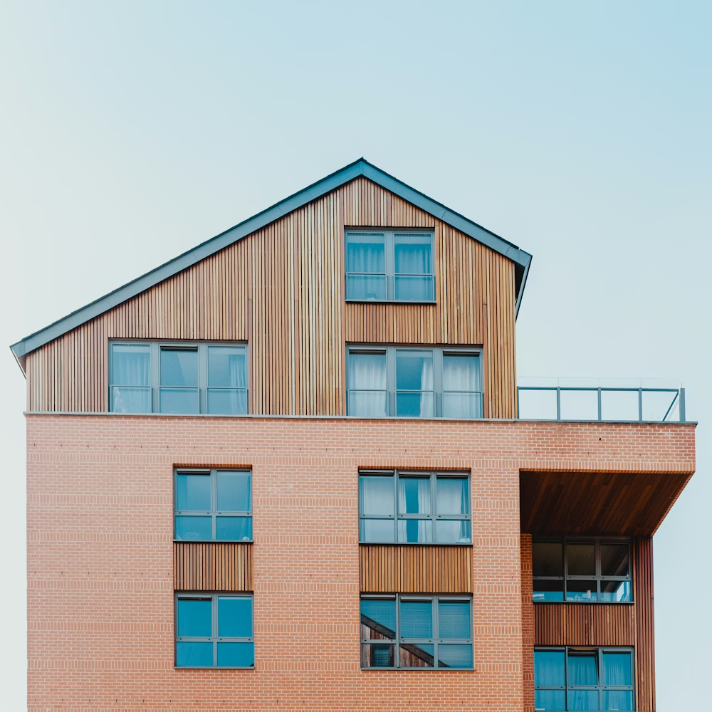 Multi-story building with brick facade and wood-paneled upper section under a blue sky.