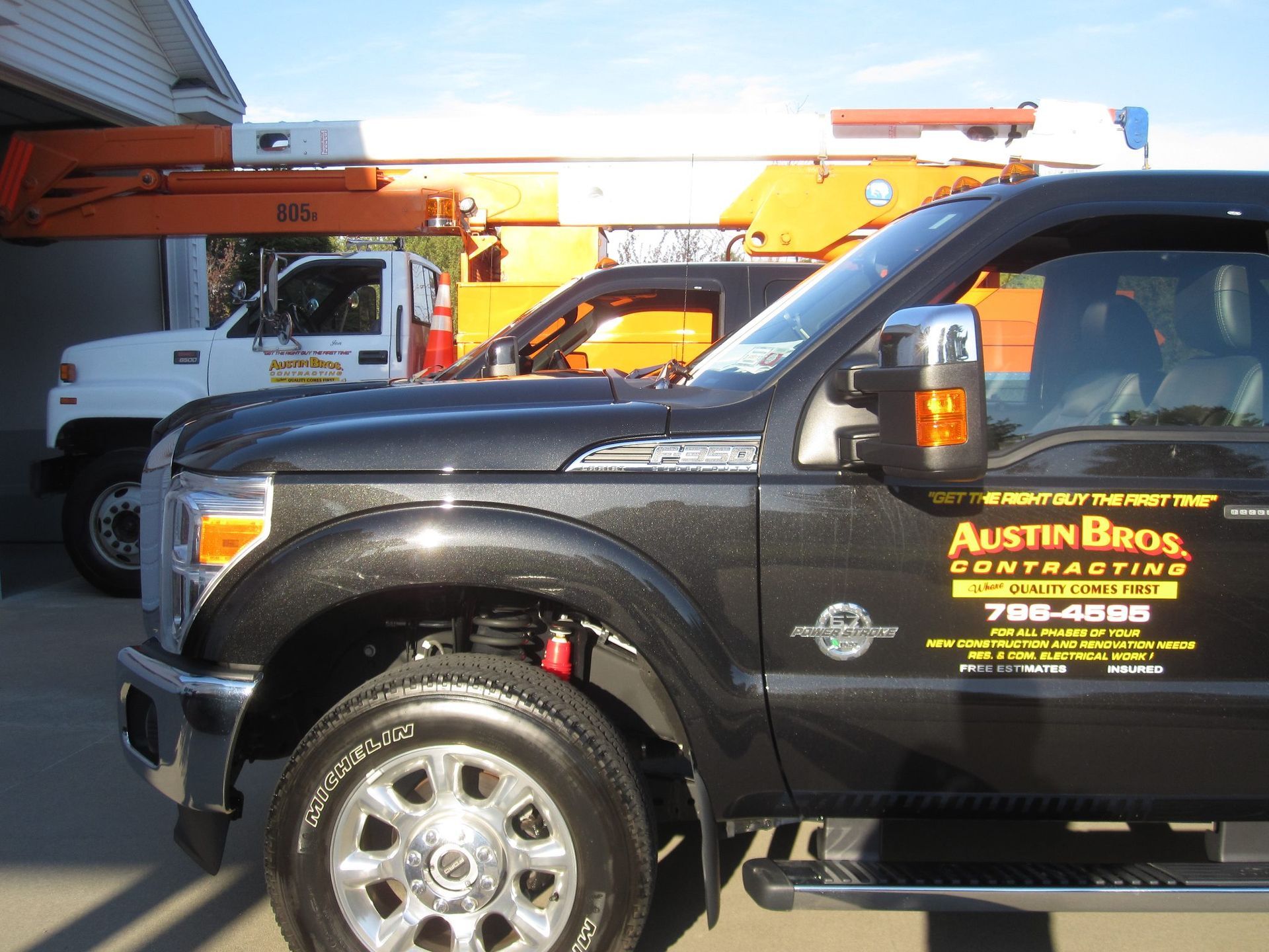 Black pickup truck with business logo parked next to white truck and orange crane in front of a building.