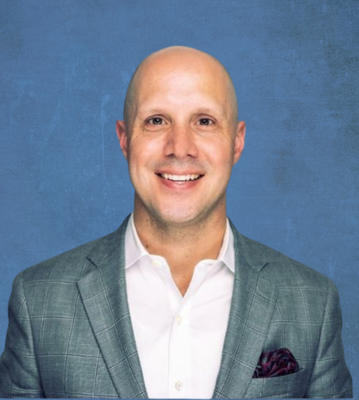 A bald man in a suit and white shirt is smiling for the camera.