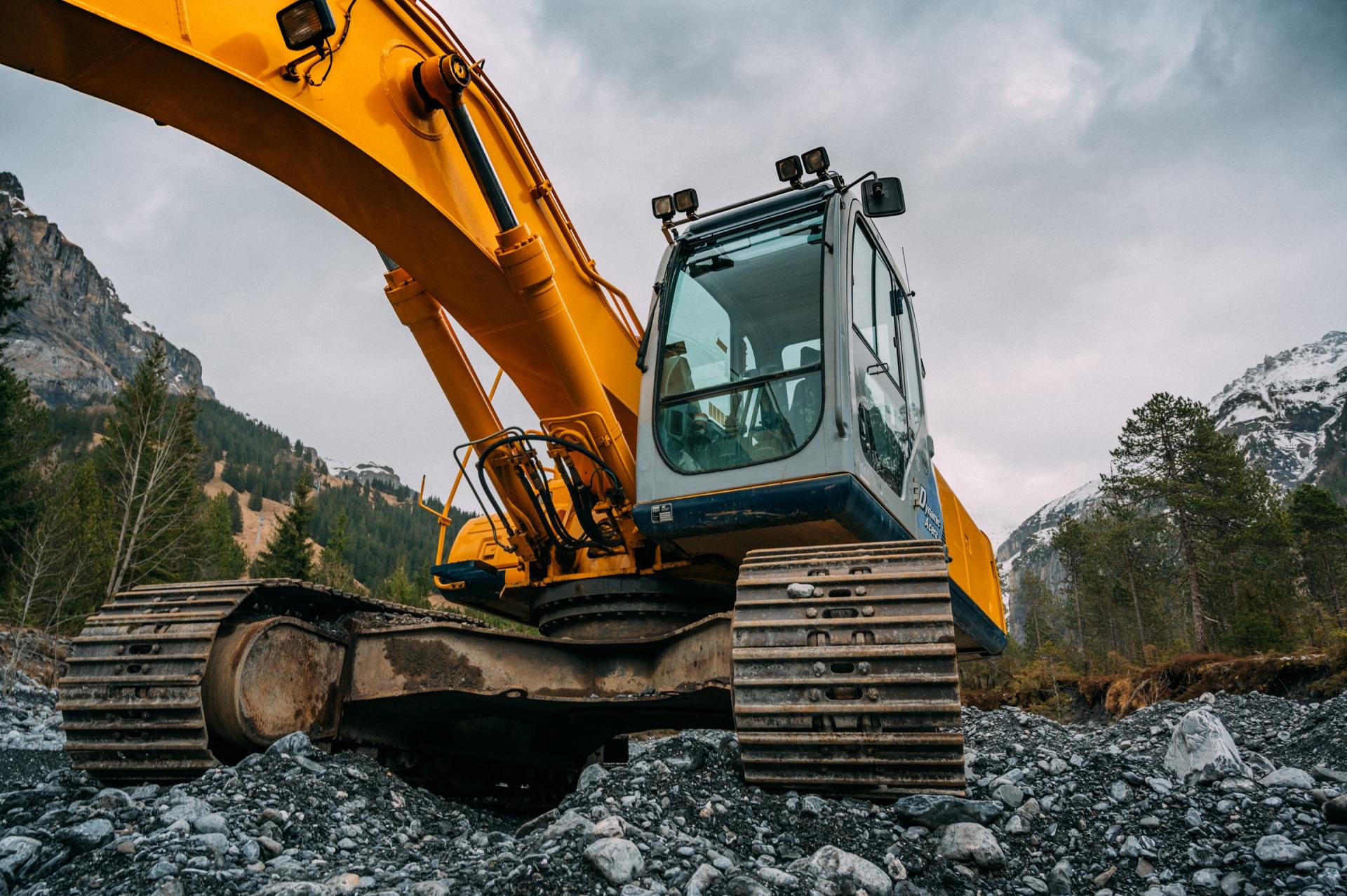 A large yellow excavator is sitting on top of a rocky hillside.