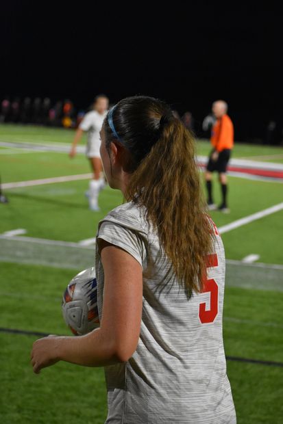 Soccer player in a gray jersey with the number 5 on her back, holding a ball on the field.