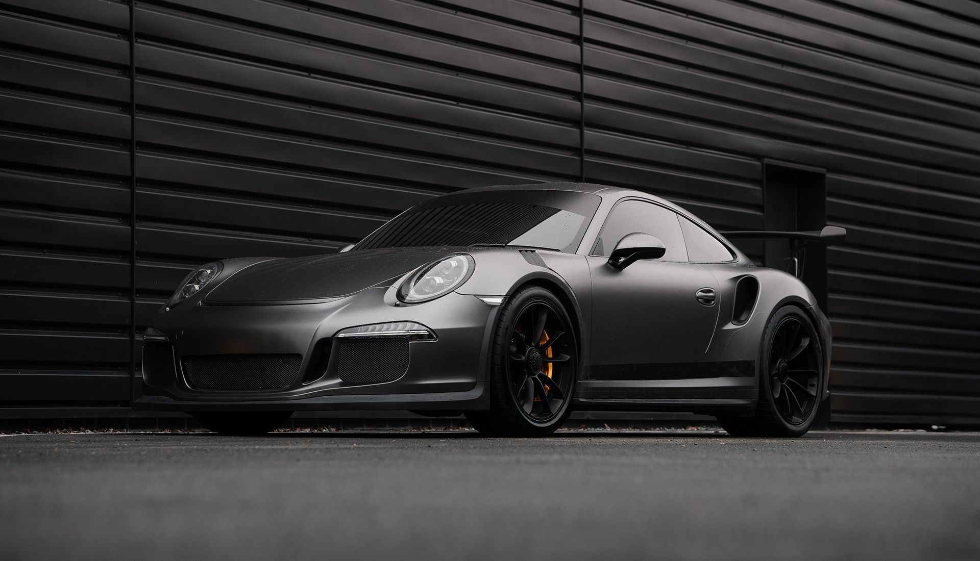 Gray Porsche sports car parked against a dark, textured wall.