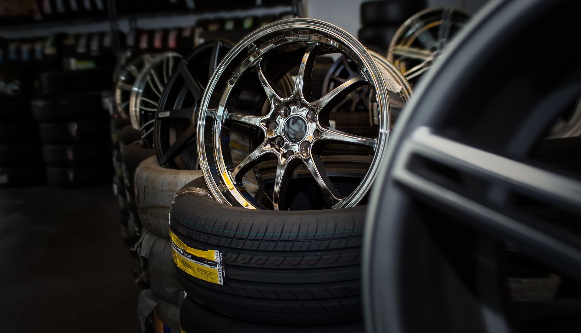 Chrome alloy wheel on top of stacked tires at a tire shop.