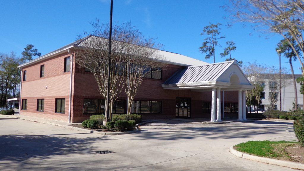 Brick building with an entrance awning, a paved area, and a sunny, outdoor setting.