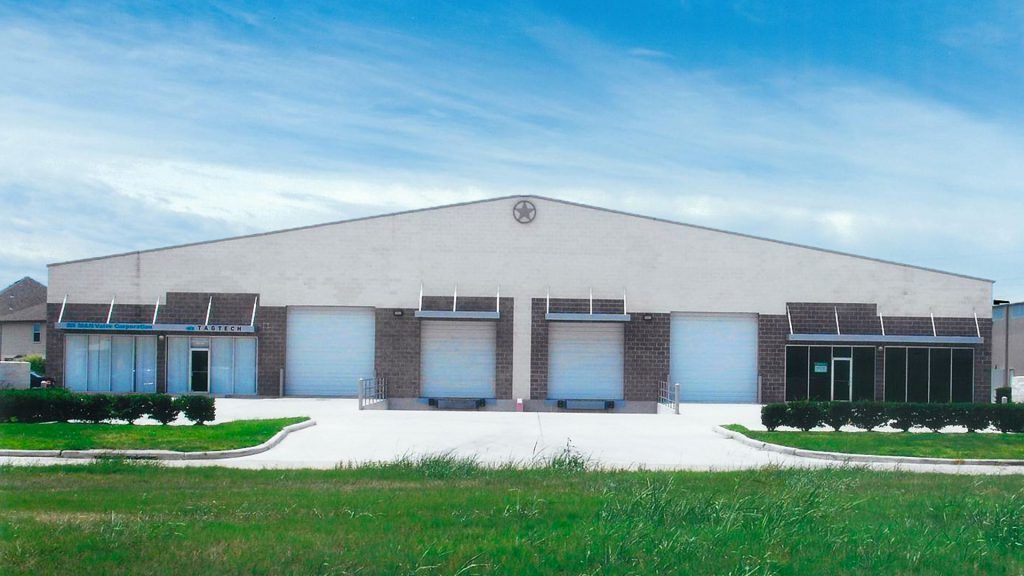 Warehouse building with loading doors, brick accents, and a cross emblem on the roof against a blue sky.