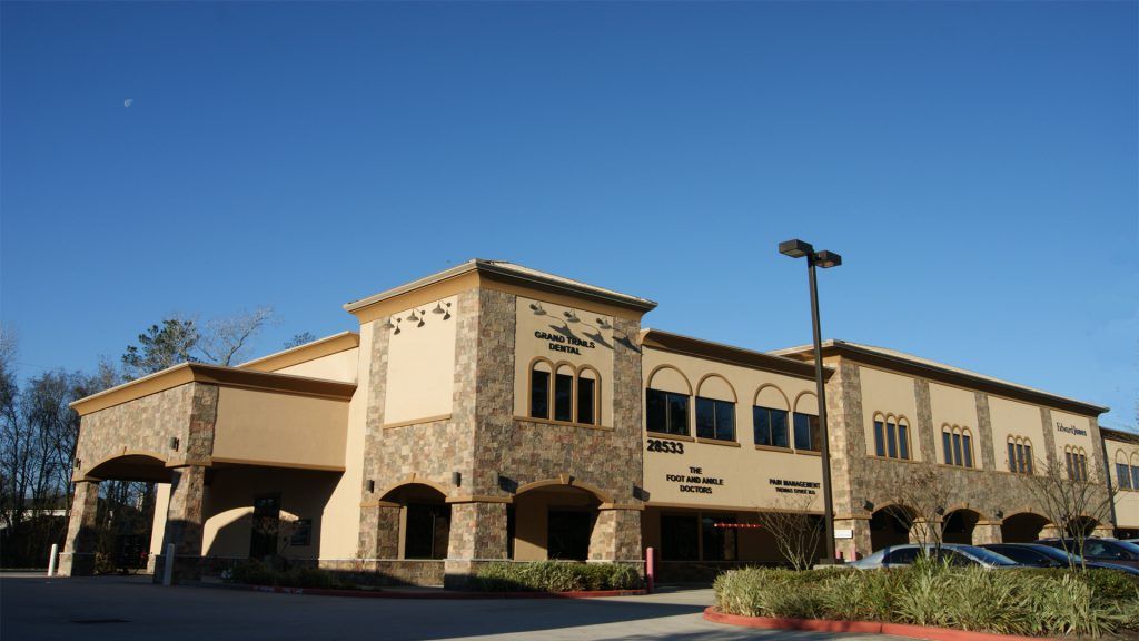 Two-story tan and stone building with arched entrance and windows against a blue sky.