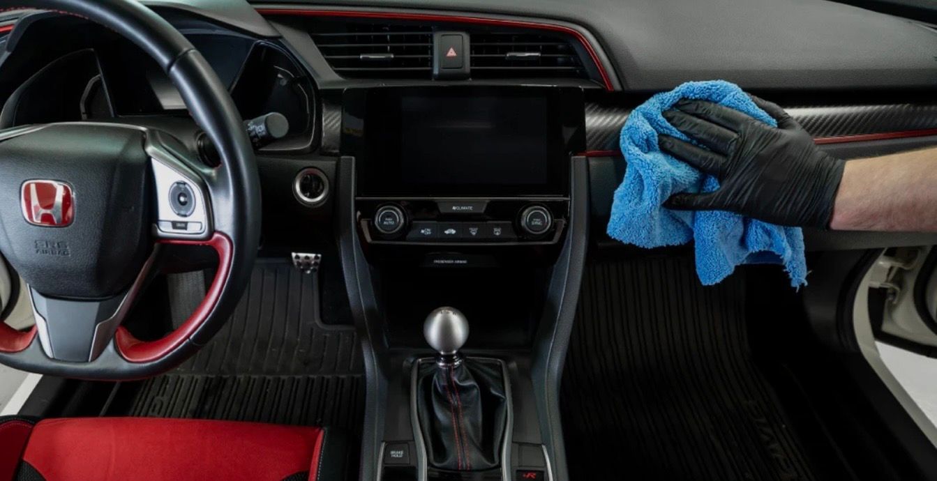 Person wearing a glove wiping the dashboard of a black and red Honda Civic with a blue cloth.