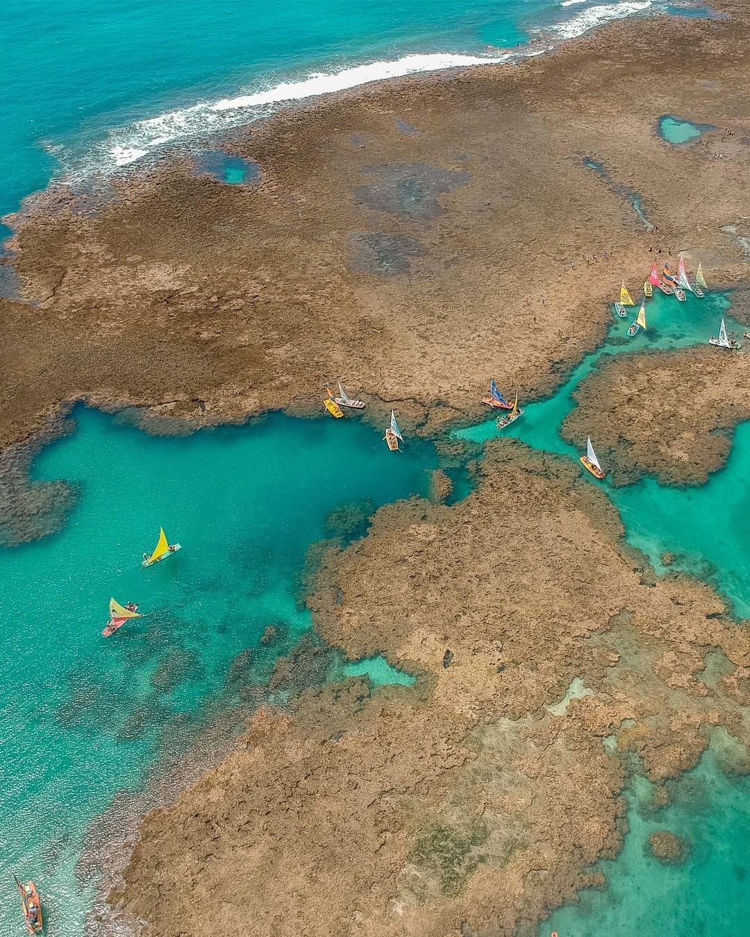 Vista aérea de barcos em uma lagoa azul-turquesa cercada por um recife de coral em uma área costeira rasa.
