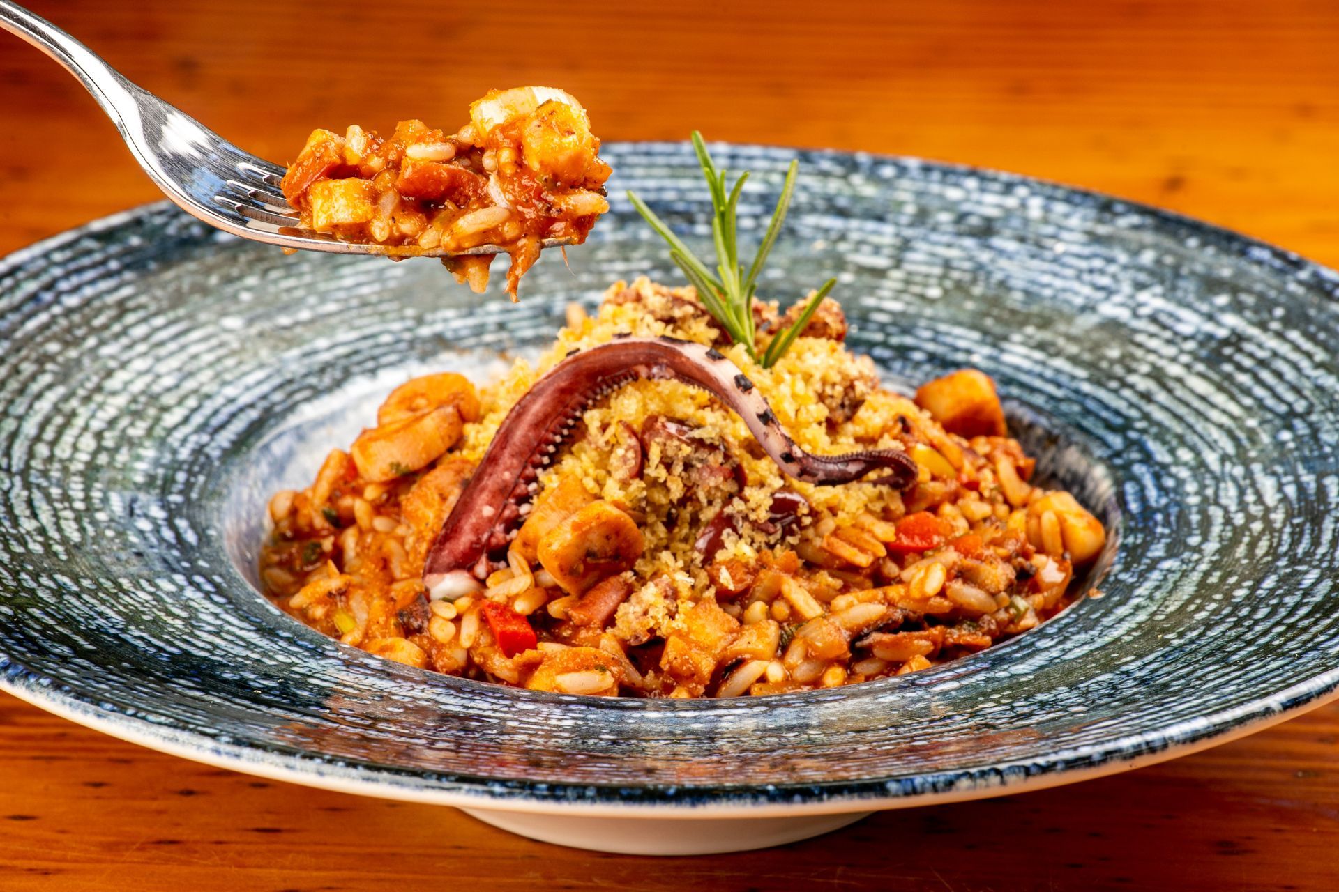 Paella com frutos do mar, servida em uma tigela azul. Uma colherada de arroz e frutos do mar sendo levantados.