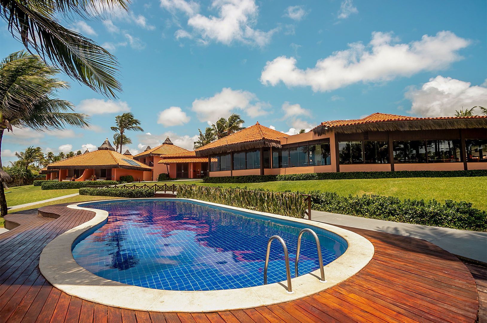Resort com piscina, restaurante e palmeiras sob um céu azul.