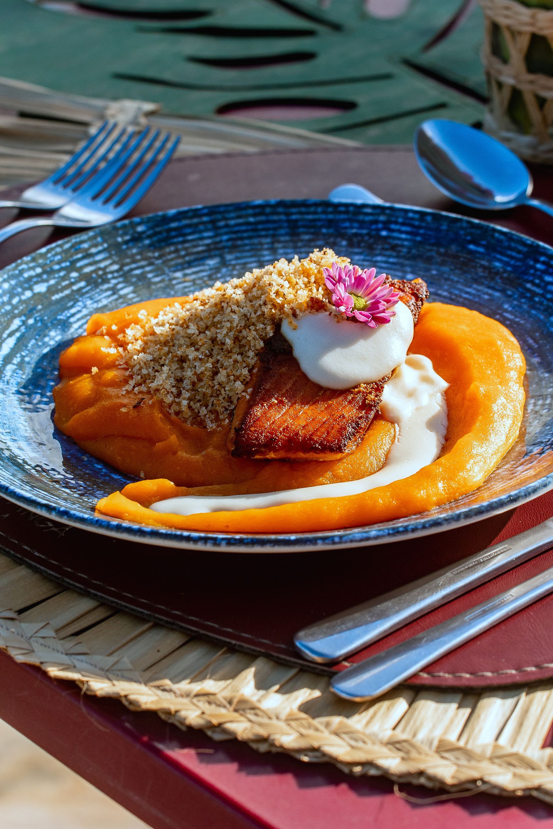 Sobremesa de abóbora em prato azul, decorada com creme, crumble e flores.