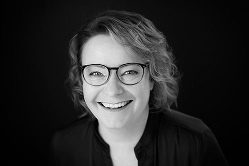 A Black and White Portrait of Karin Kuschel, a smiling woman with glasses