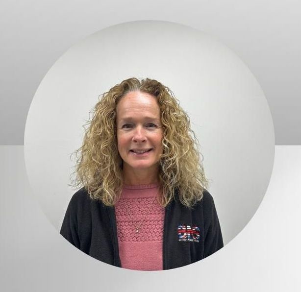 A woman with curly hair is wearing a pink sweater and a black jacket.