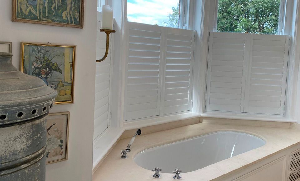 A bathroom with a bathtub and shutters on the windows.