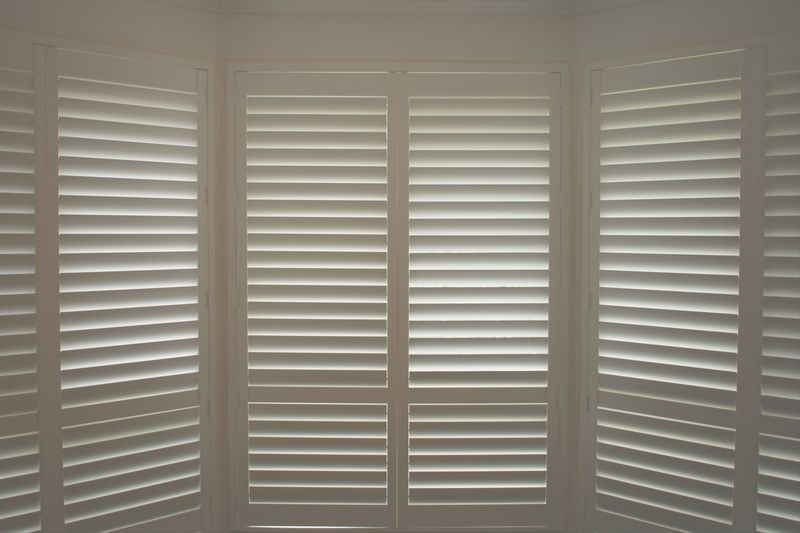 A window with white shutters on it in a room.